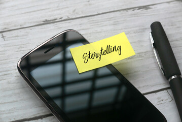 Selective focus of pen, mobile phone and sticky note written with Storytelling on white wooden...