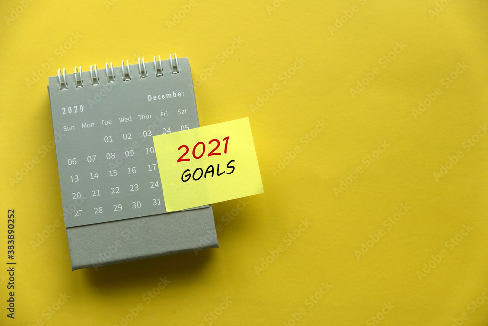 Poster top view of december 2020 calendar with sticky note written with 2021 goals on yellow background wit