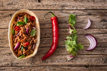 Mexican barquita taco with beef, chilli, tomato, onion and spices on wooden table. Top view	