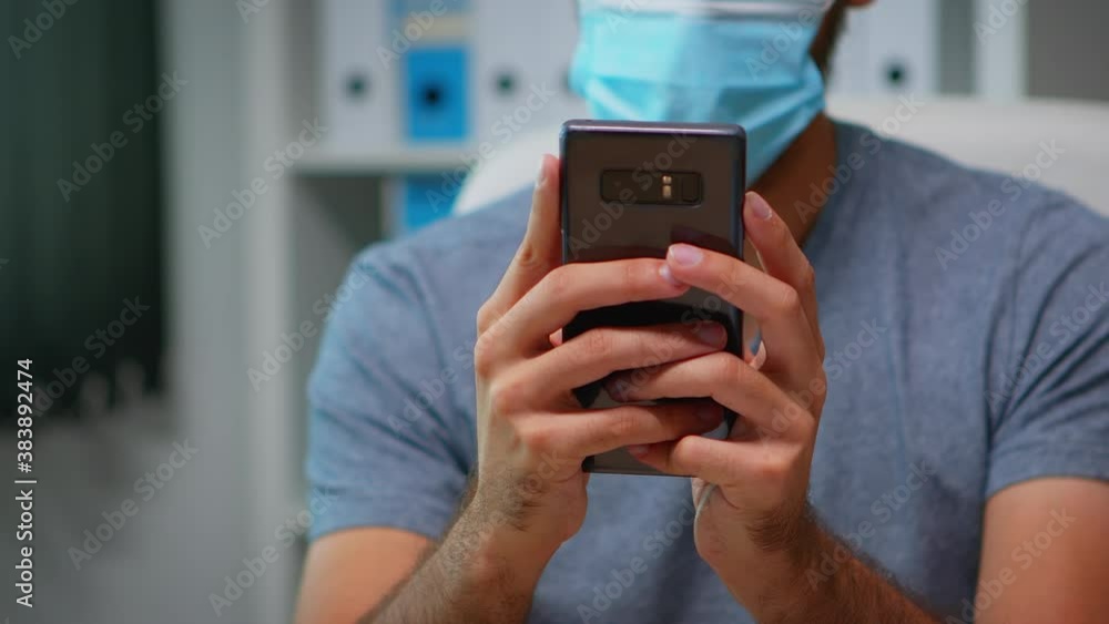 Poster close up of man with face mask typing text messages on smartphone sitting in workplace during corona