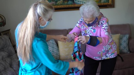 Elderly woman wearing face mask holds bathing suits up showing them to friend daughter in her living room. Concept of smiling active elderly woman excited to try on aqua aerobics suit.
