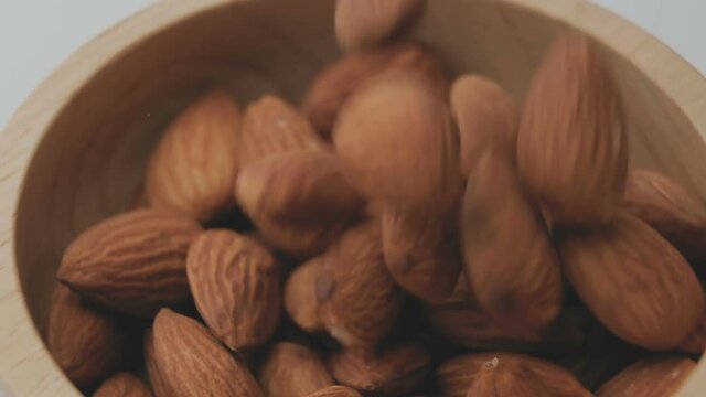slow motion macro of roasted almond seeds falling down into wooden bowl