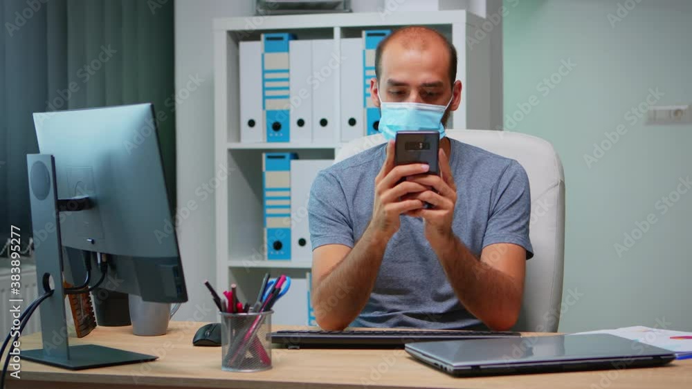 Poster office worker with protective mask using phone typing sitting on modern office during coronavirus. f