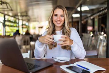 Fototapeta na wymiar Beautiful happy woman working on laptop computer during coffee break in cafe shop