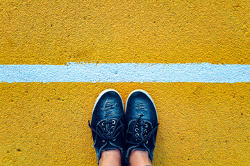 Top view of female legs standing next to the white line on yellow background.