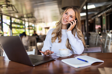 Portrait of pretty woman talking on the phone while sitting in the cafe and enjoying coffee