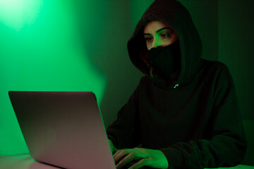 Gamer  playing video games while she is wearing face mask during lockdown.
Hacker working on laptop while she is wearing face mask in a dark room with green light.