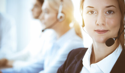 Call center and business people concept. Beautiful business woman with headphones consulting clients. Group of diverse phone operators at work in office