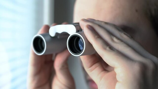 Man with binoculars. Private detective, agent or investigator looking out the window. Man spying or investigating. Privacy, surveillance or espionage concept. Suspicious or curious person spying.