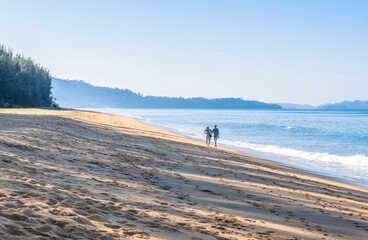 A man and a woman walk along the edge of the sea on the beach early in the morning