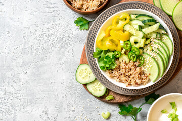 Burrito bowl with quinoa and green vegetables. Quinoa, cucumber, pepper, radish and celery in a bowl on a gray background top view. Free space for text. Healthy diet food, vegetarian food. Copy space