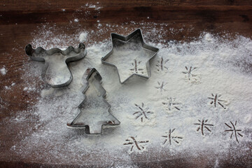 Reindeer, christmas tree and star gingerbread cookie cutters and flour like a snow on wooden background. Christmas food background. Top view, copy space