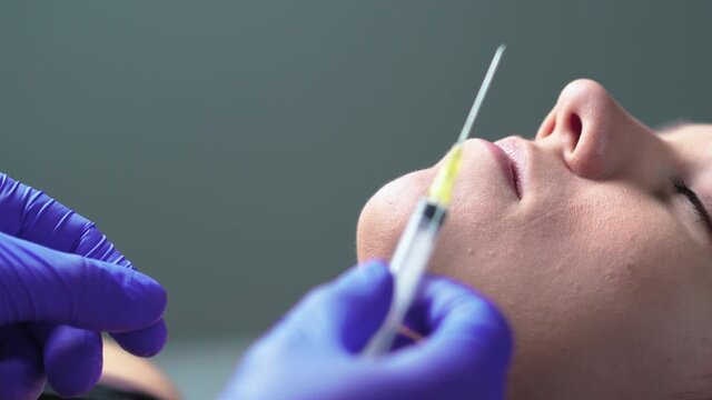 Plastic surgery, lip injection and augmentation or beauty treatment concept. Doctor with gloves and filler needle and syringe preparing injecting lips for woman. Cosmetic procedure in salon or spa.