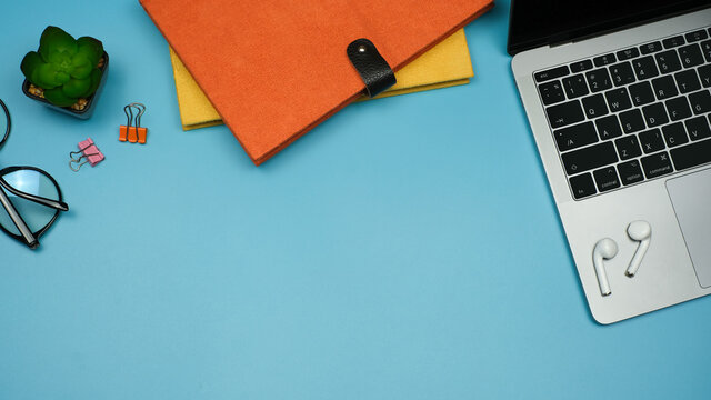Flat lay, Workspace back to school and education concept on blue table desk background with laptop compute and stack of book, earphone, green plant and eyeglass, Top view with copy space