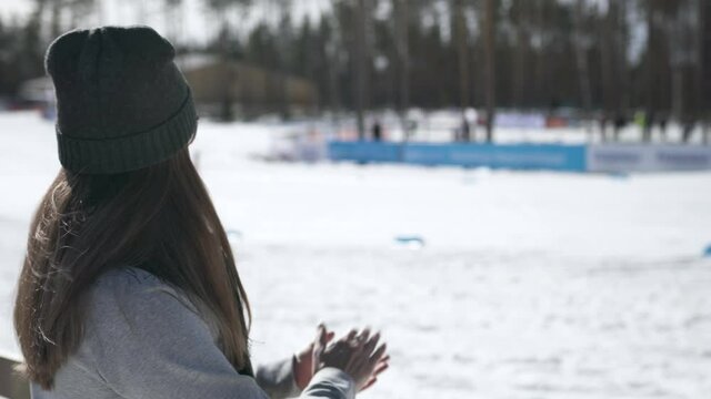 Fan cheering in skiing competition. Winter olympics or world championship event. Woman watching cross-country skier competing in stadium. Crowd supporting athlete.