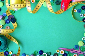Frame on a green background consisting of buttons and colored threads, scissors, a thimble and a yellow measuring tape