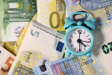 Small blue retro alarm clock on a euro banknotes background. Finance. Financial crisis. Banking system. Economic problem. Inflation. Money printing.