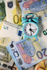 Small blue retro alarm clock on a euro banknotes background. Finance. Financial crisis. Banking system. Economic problem. Inflation. Money printing.