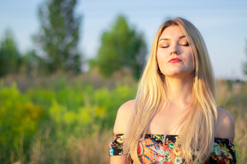 overlight bright portrait of a charming attractive blonde in flowery dress in the field.  - obrazy, fototapety, plakaty