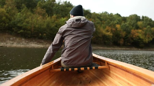 Rear view of man paddling canoe on the rainy forest lake