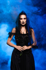 bride in black dress and veil on blue with smoke, halloween concept