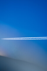 Aircraft on clear sky with white smoke trails, cold tone