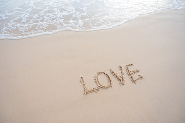 Fototapeta premium The word LOVE written on sand beach with soft wave