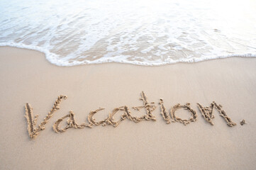 The word Vacation written on sand beach with soft wave