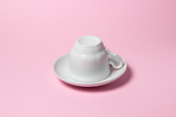 Upside down coffee cup on a pink background. Coffee cup and saucer.