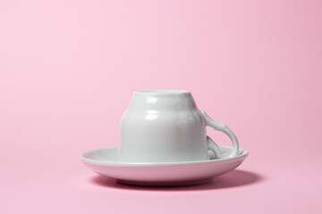 Upside down coffee cup on a pink background. Coffee cup and saucer.