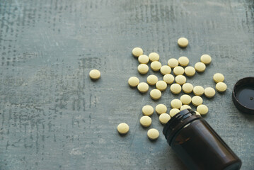 yellow round tablets or pills vitamins on blue stone concrete table with black plastic bottle, side angle view from above, horizontal stock photo image background with copy space