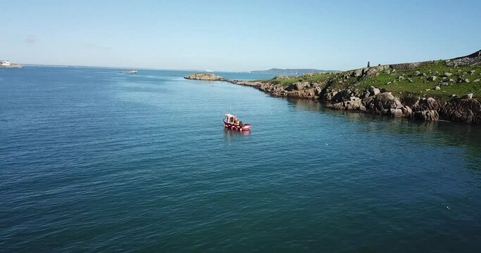 Aerial footage of red fishing boat off Dalkey Island on sunny day.