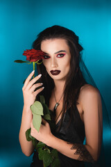 Naklejka premium young woman with dark makeup holding red rose on blue