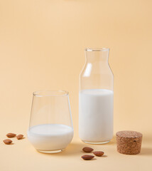 a glass and bottle of  vegan almond milk and a few scattered nuts on a yellow  background
