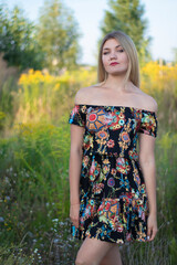 Fototapeta premium overlight bright portrait of a charming attractive blonde in flowery dress in the field. 