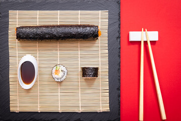 Présentation de plat de cuisine Japonaise, sushi et maki sur fond noir avec sauce soja et baguettes.	