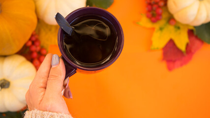 Hand holding cup of tea over the orange halloween background with pumpkins and autumn leaves . Autumn thanksgiving decoration with copy space. Halloween concept.