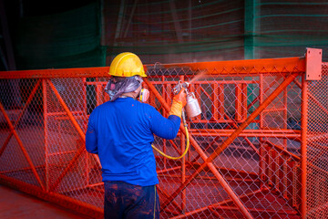 The painter is working to painting the steel structure with spray gun, at industrial factory.