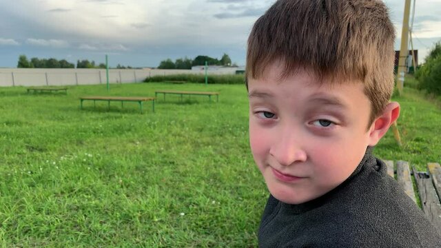 A boy sitting on a bench on a children playground, looking in a camera and making funny faces using his eyebrows