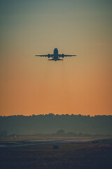Passenger aircraft short after take off in evening lights. Airplane above airport runway at sunset. Dark, soft, dreamy colors