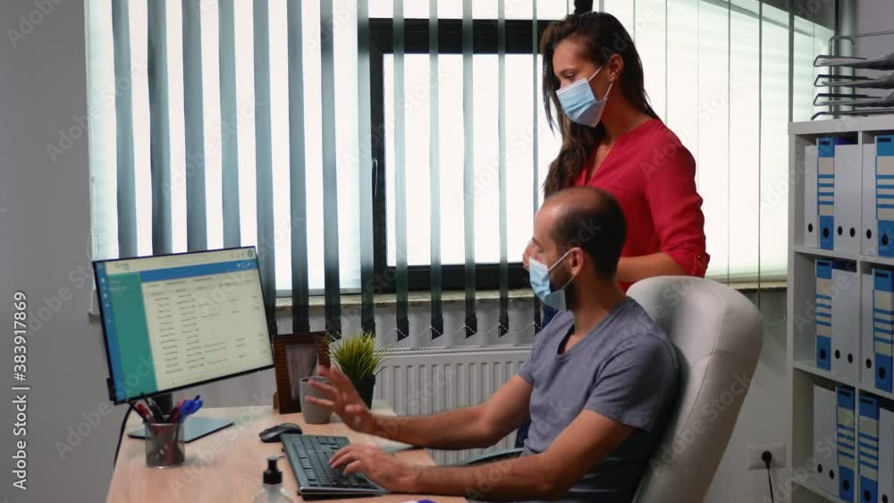 Poster man with protection mask showing clients list on computer sitting in office room. employees working 
