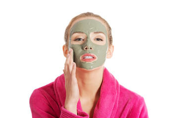 Beautiful woman in pink bathrobe and havinf facial mask.
