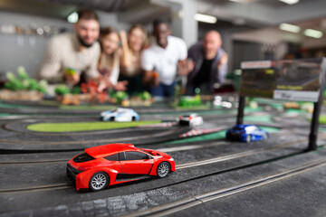 Cheerful smiling men and women play together with the slot car racing track