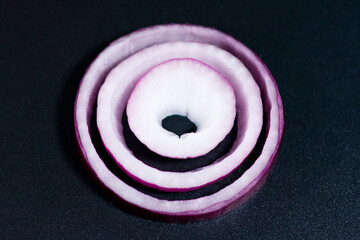 Fototapeta na wymiar Slices of sliced onion rings on a dark background. Closeup.