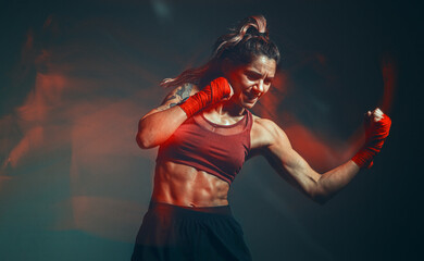 Cool female fighter in boxing bandages trains in studio in red neon light. Mixed martial arts. Long exposure shot