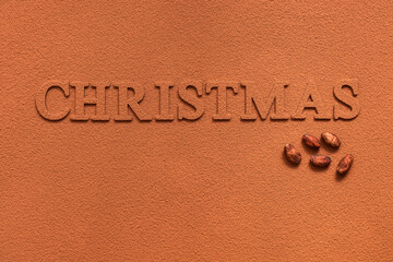 Fototapeta na wymiar Christmas lettering sprinkled with cocoa powder and cocoa beans on a background of cocoa powder. Top view, flat lay. Abstract background.