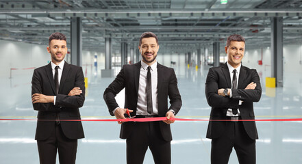 Businessmen cutting a red ribbon tape and opening a factory