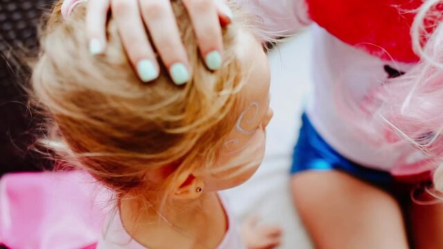 Female animator making face painting for a young blond girl at the kid's party. Focus is at the girl. Slow motion video.