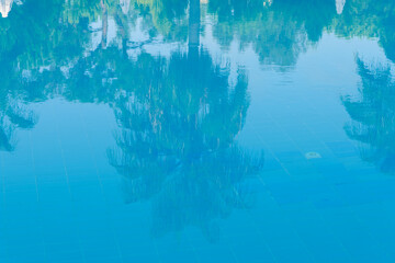Fototapeta premium Reflections of palm trees in the calm blue water of a swimming pool conceptual of tropical summer vacations and travel