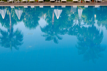 Reflections of palm trees in the calm blue water of a swimming pool conceptual of tropical summer vacations and travel